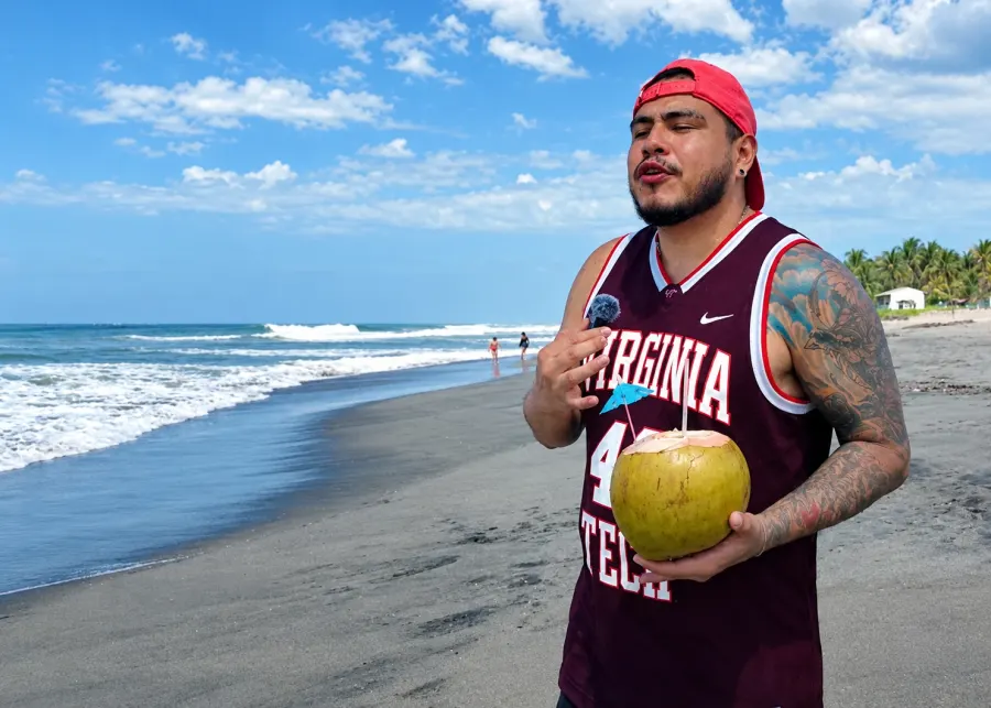 Viajero en la playa sosteniendo un coco frente al mar